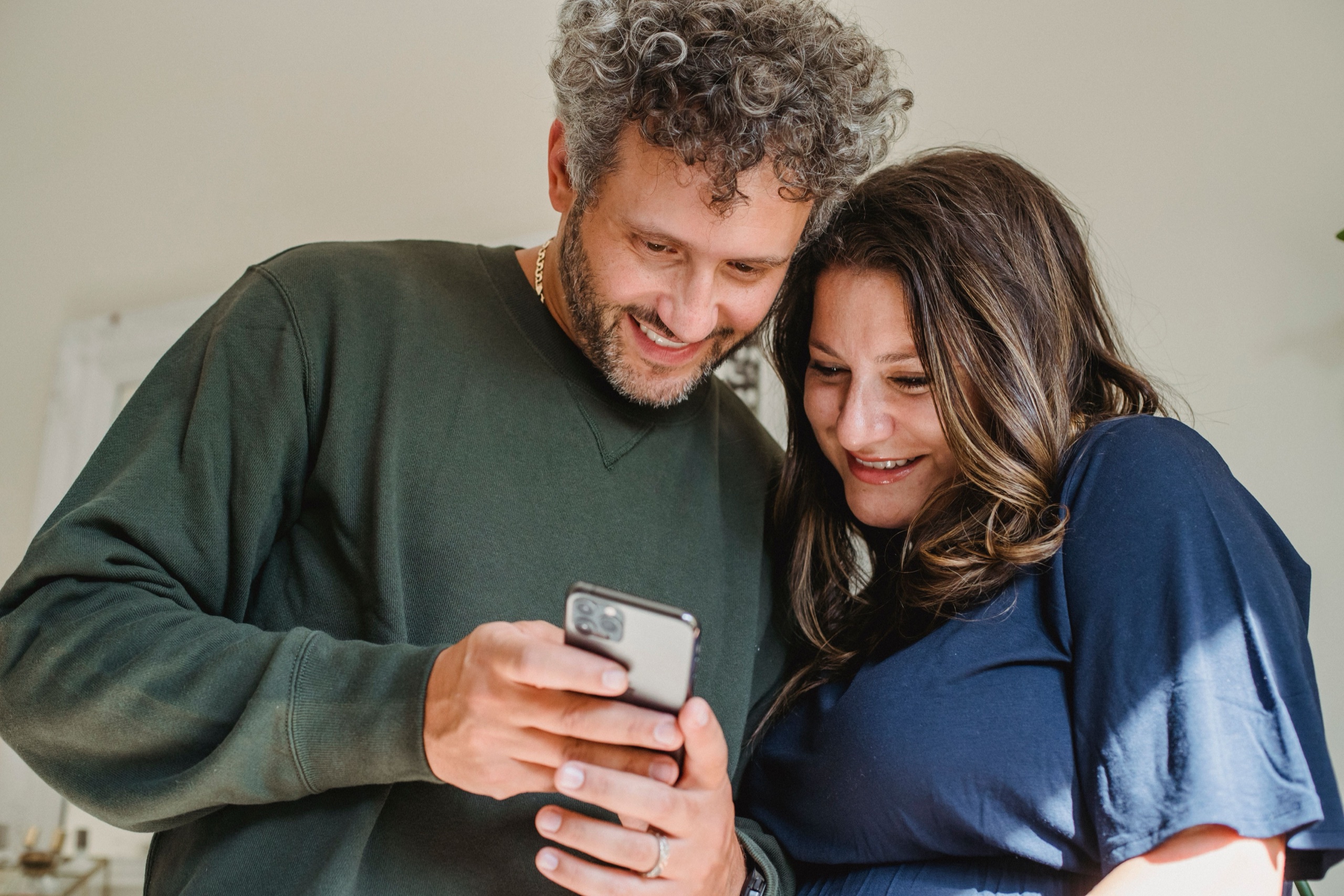 A couple smiling as they look at a phone together at home